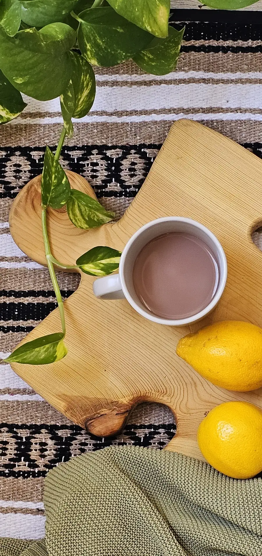 Tasse Kakao auf einem Holzbrett, daneben Zitronen und eine Zimmerpflanze